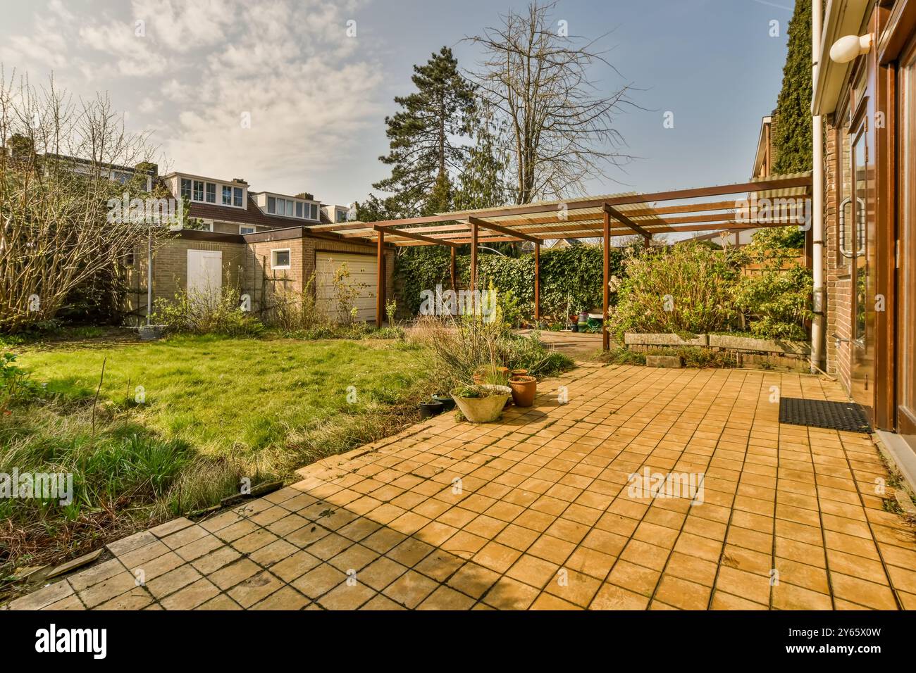 Une cour arrière bien entretenue avec une grande pergola en bois, patio carrelé et diverses plantes vertes sous un ciel ensoleillé. Banque D'Images