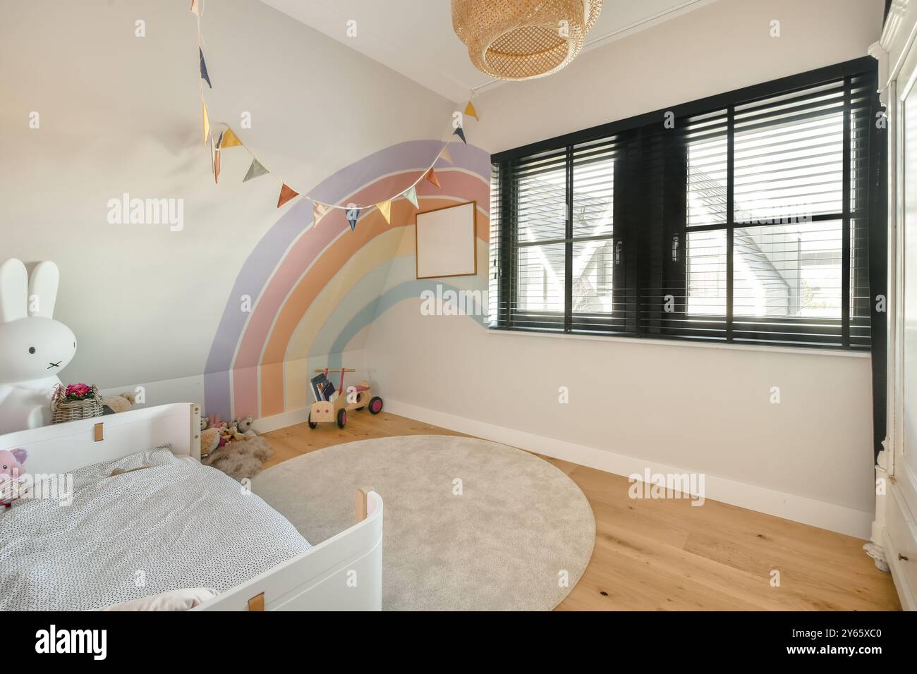 Une chambre accueillante pour enfants est décorée d'une fresque arc-en-ciel pastel, d'un berceau blanc, de jouets en peluche et d'une guirlande décorative. Banque D'Images