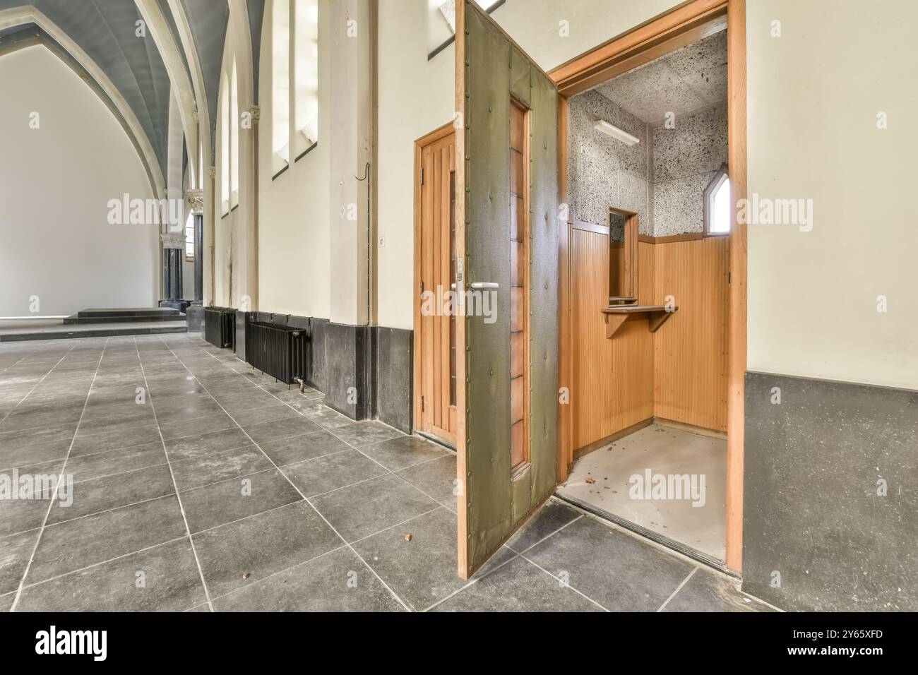 'Couloir poussiéreux dans un bâtiment abandonné avec des arches de style gothique et une porte en bois ouverte menant à une petite pièce.' Banque D'Images