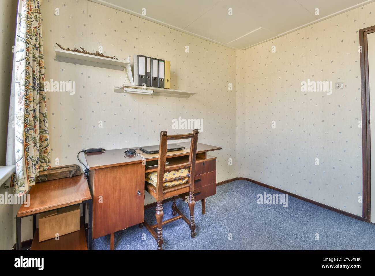 Un bureau à domicile à l'ancienne doté d'un bureau classique en bois avec tiroirs, rideaux fleuris et deux étagères avec des classeurs, sur une bande murale à motifs Banque D'Images