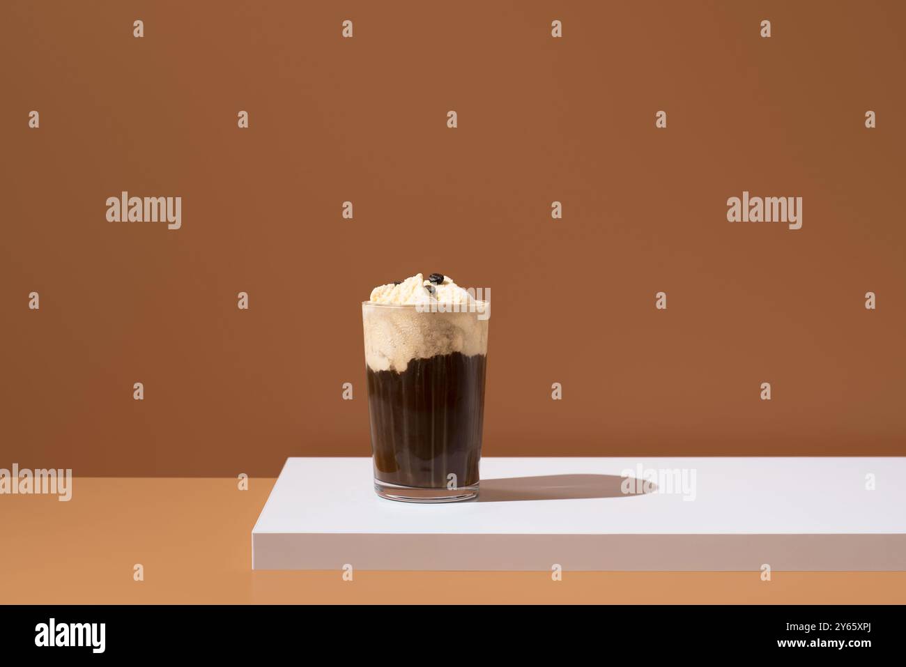 Un élégant dessert affogato avec une boule de glace à la vanille trempée dans un café riche, présenté sur une surface blanche propre avec un fond brun chaud Banque D'Images