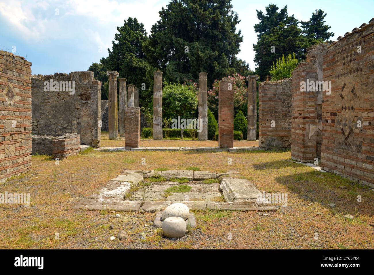 Explorez les ruines historiques de Pompéi avec d'anciennes colonnes de pierre et des murs de briques partiellement préservés au milieu d'une végétation luxuriante, capturant l'essence Banque D'Images