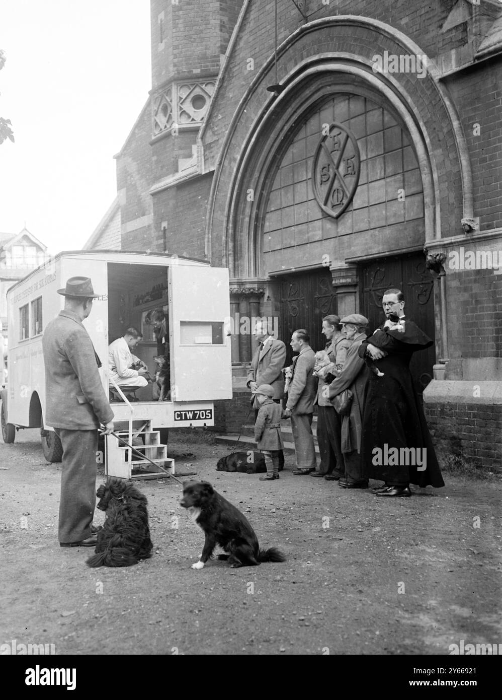 Le vicaire offre un cimetière pour la clinique des animaux sans-abri lorsque le dispensaire du peuple pour la clinique des animaux malades de Willesden a dû fermer pour réparations , le vicaire de l'église locale , St Andrews , Willesden Green a offert de laisser la PDSA mettre une de leurs ambulances mobiles dans le cimetière afin que les gens du district puissent continuer à faire traiter leurs animaux de compagnie . Photo montre : une vue générale de la scène alors que les gens , y compris le Rev G l Carpenter , curé de St Andrews , font la queue avec leurs animaux à l'ambulance mobile. 12 octobre 1950 Banque D'Images