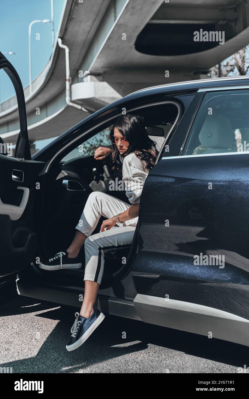 Beauté en voiture. Attrayant jeune femme élégante dans des lunettes sortant de sa voiture Banque D'Images