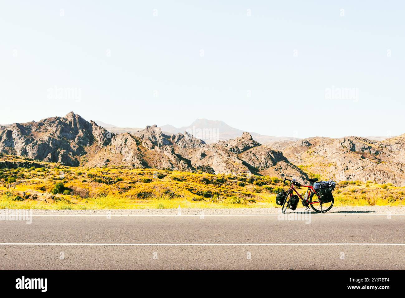 Chargé de sacs, des stands de vélo rouges sur le côté de la route entourée de vaches dans une campagne du parc national de Kazbegi. Vacances à vélo. Banque D'Images