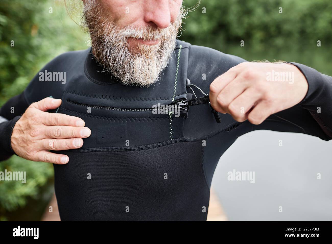 Gros plan de l'homme barbu mûr enfilant une combinaison au bord du lac et fermant les fermetures velcro se préparant pour la plongée Banque D'Images