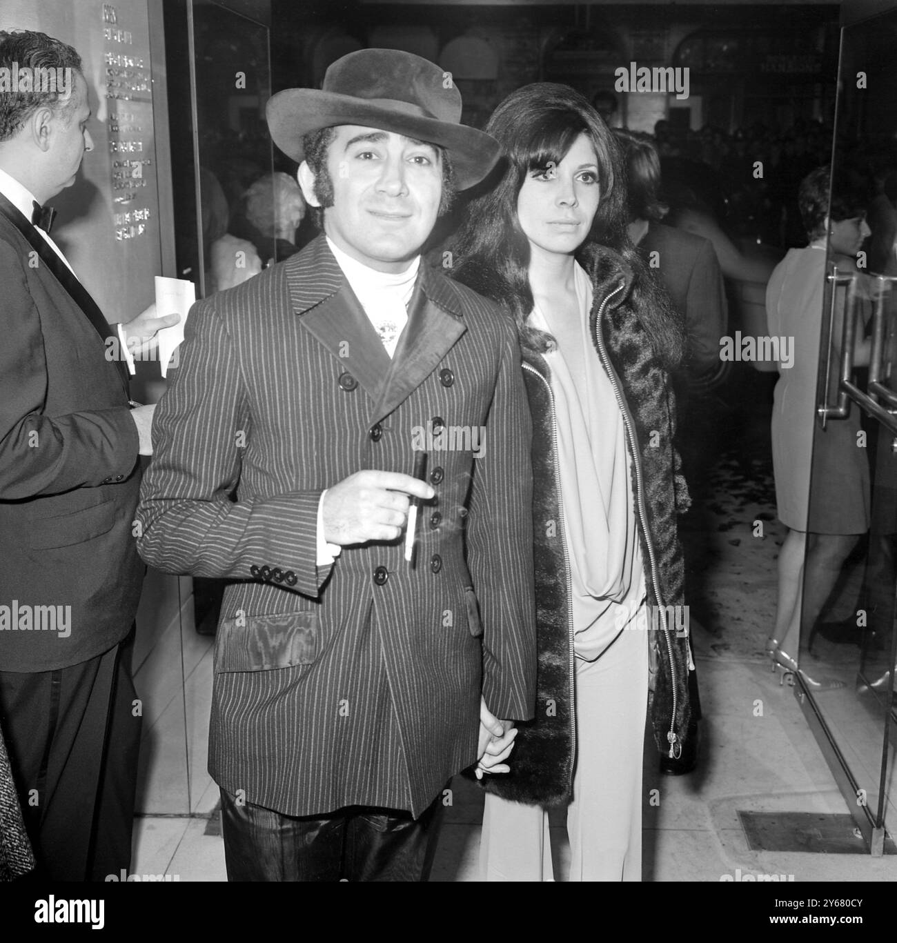 Lionel Bart et sa compagne Sharon Sheeley arrivent à la première de 'Third Modern Millie. Lionel portait un manteau double croisé rayé très boutonné avec revers et rabats de poche qui correspondent à son pantalon, Sharon porte un pantalon de pyjama blanc avec encolure plongeante 13 octobre 1967 Banque D'Images