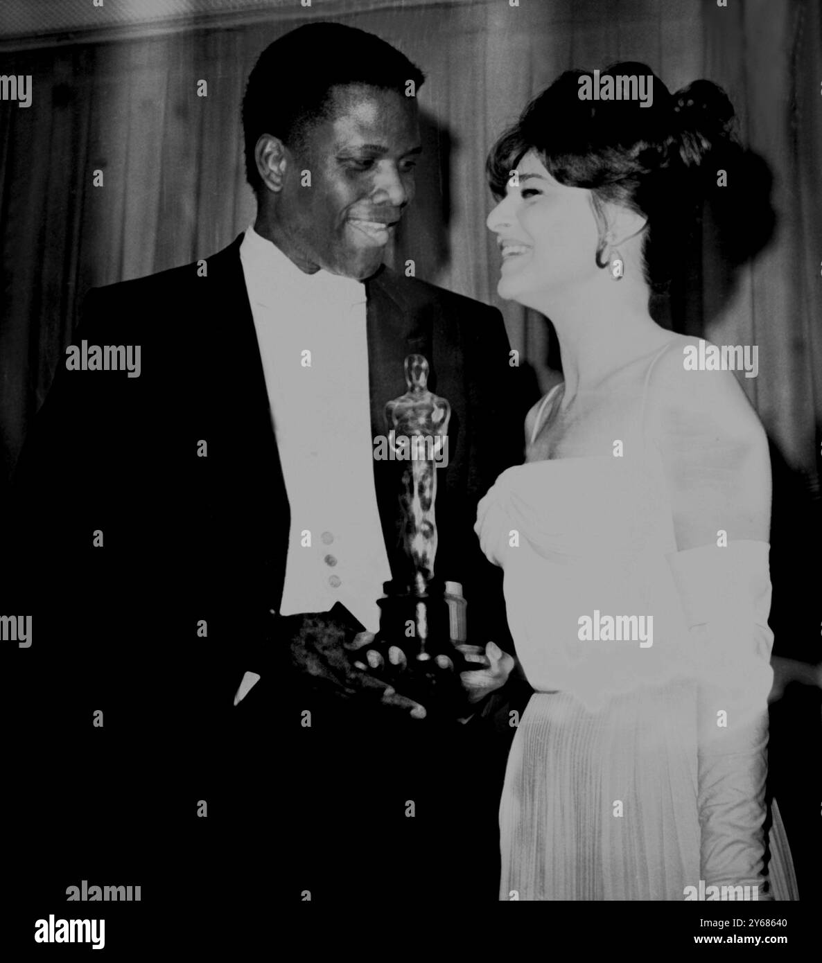 L'acteur Sidney Poitier avec Anne Bancroft après qu'elle lui ait remis son Oscar du meilleur acteur de l'année. Mlle Bancroft a été actrice de l'année dernière. Poitier, le premier homme noir à remporter le prix du meilleur acteur, a reçu les honneurs pour son rôle dans « Lys of the Field ». - 16 avril 1964 - Santa Monica , Californie , États-Unis Banque D'Images