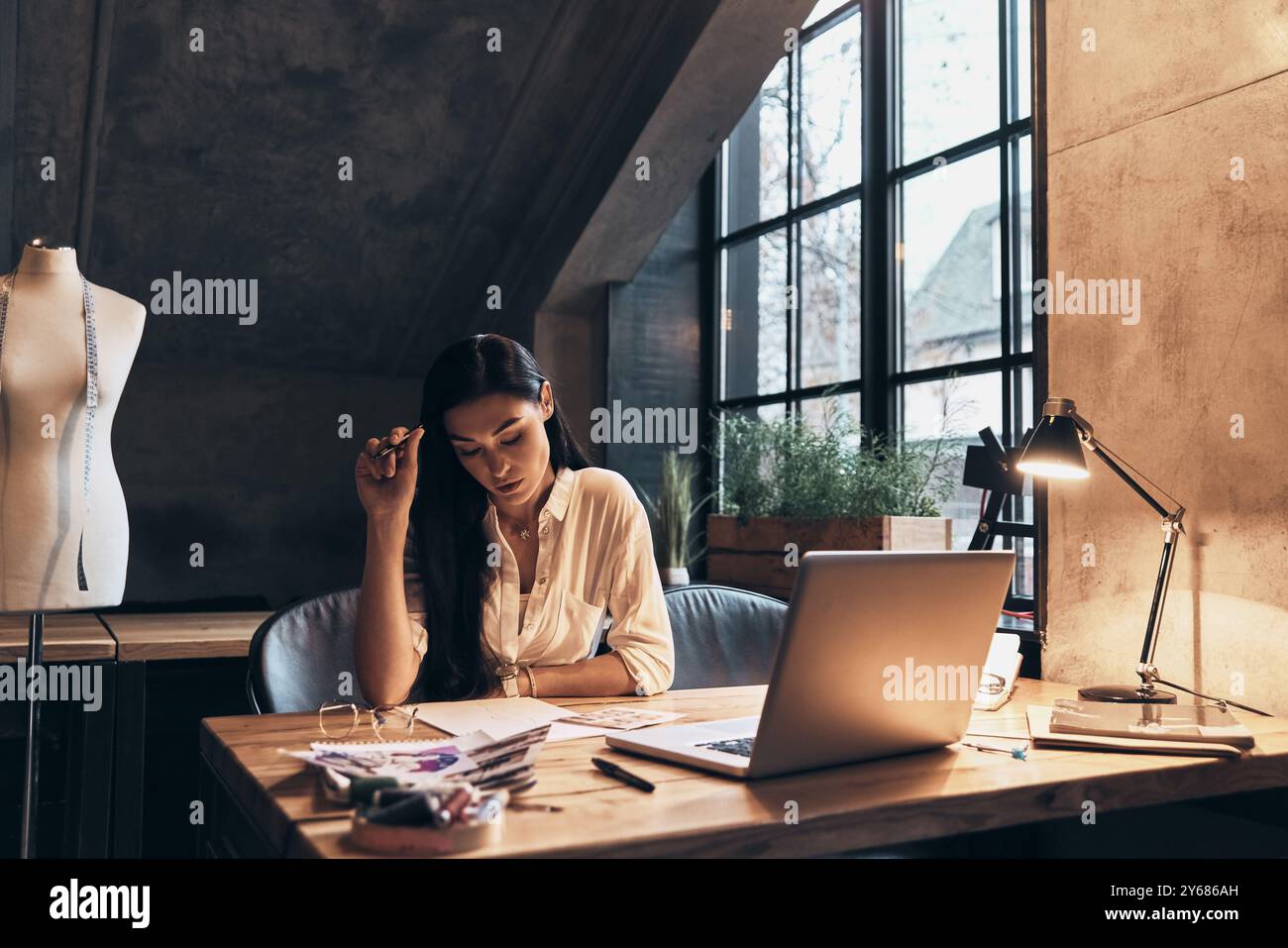 Transformer les idées en vêtements. Belle jeune femme travaillant sur des croquis tout en étant assise dans son atelier Banque D'Images