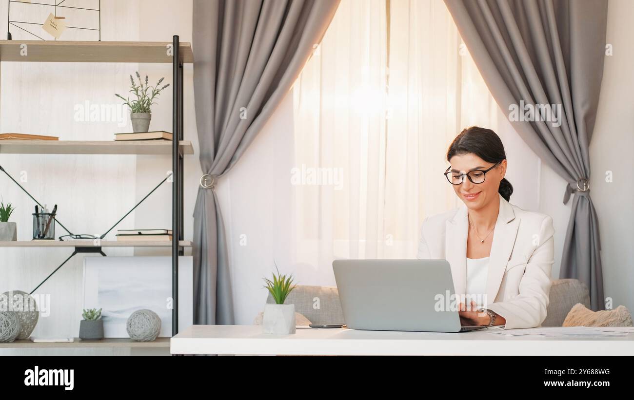 Travailler avec plaisir. Femme élégante. Communication professionnelle. Heureuse dame élégante tapant ordinateur portable bureau assis dans l'intérieur de la salle de bureau léger. Banque D'Images