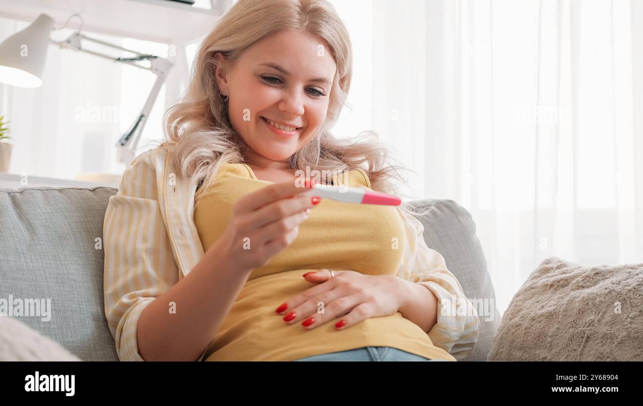 Joie de grossesse. Femme excitée. Résultat prometteur. Dame joyeuse regardant sur le résultat positif de test médical assis intérieur de la salle de lumière. Banque D'Images