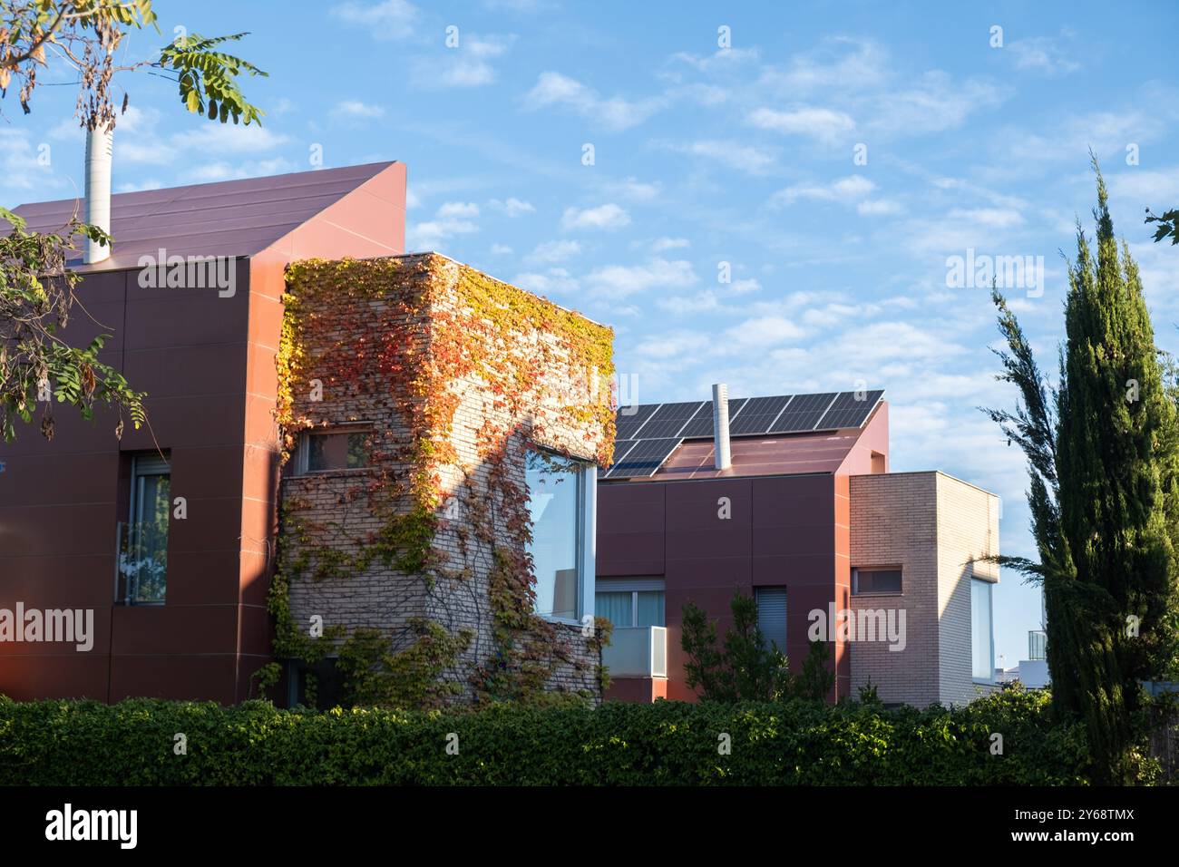 Il se lève dans un quartier résidentiel avec des panneaux solaires photovoltaïques pour produire de l’énergie impie et renouvelable. C'est l'automne, les feuilles sont rougeâtres et le ciel Banque D'Images