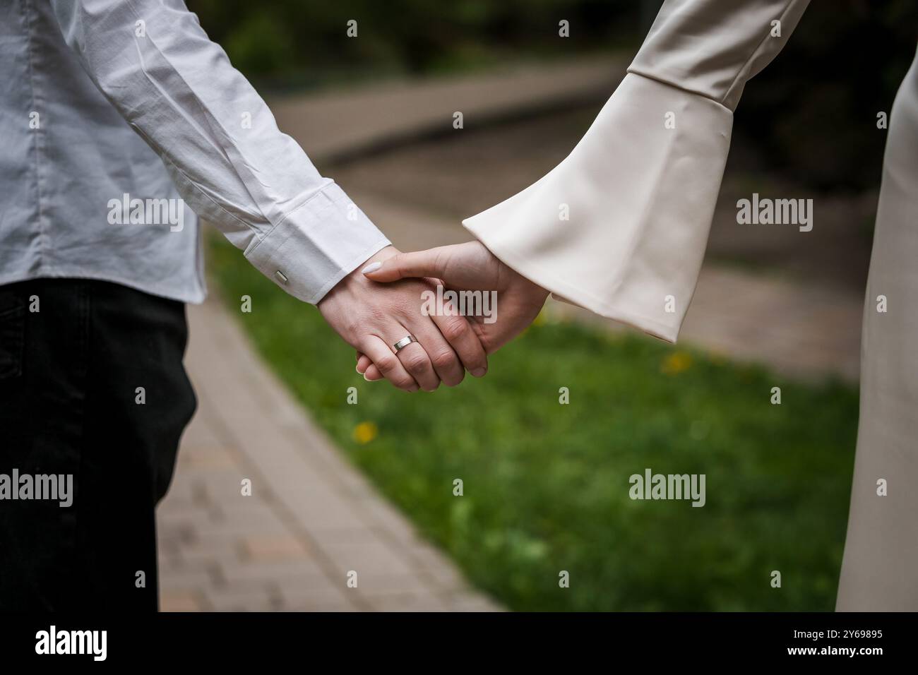 Gros plan romantique des mains entrelacées de mariée et mariée sur un chemin serein. Banque D'Images