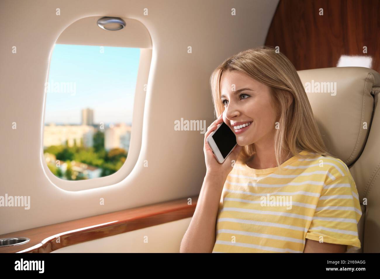 Femme parlant au téléphone dans la cabine pendant que l'avion décolle ou atterrit, vue sur la ville depuis la fenêtre Banque D'Images