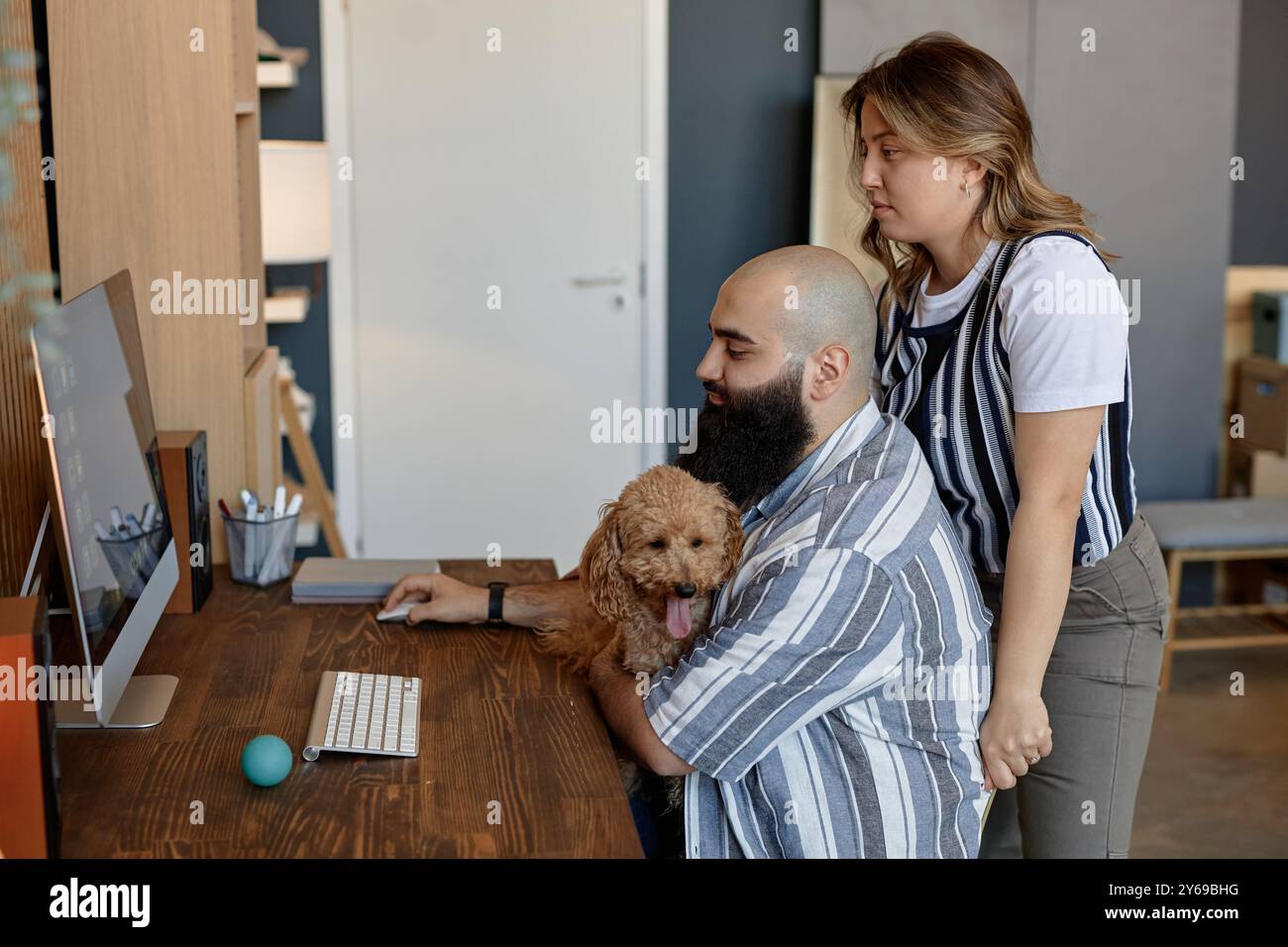 Deux collègues collaborant sur le projet au bureau à domicile avec un chien de compagnie à côté d'eux personne assis au bureau travaillant sur l'ordinateur tandis qu'un autre se tient debout fournissant des commentaires Banque D'Images