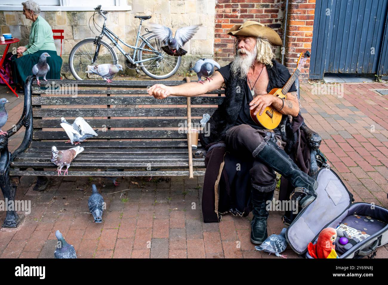 Un artiste de rue en costume de pirate est assis sur Un banc public nourrissant des pigeons, High Street, Lewes, Sussex, Royaume-Uni. Banque D'Images