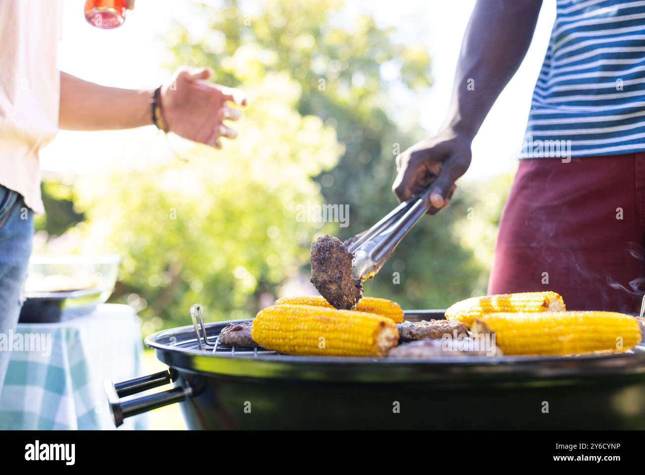 Griller du maïs et des hamburgers, deux amis masculins divers profitant d'un barbecue en plein air ensemble Banque D'Images