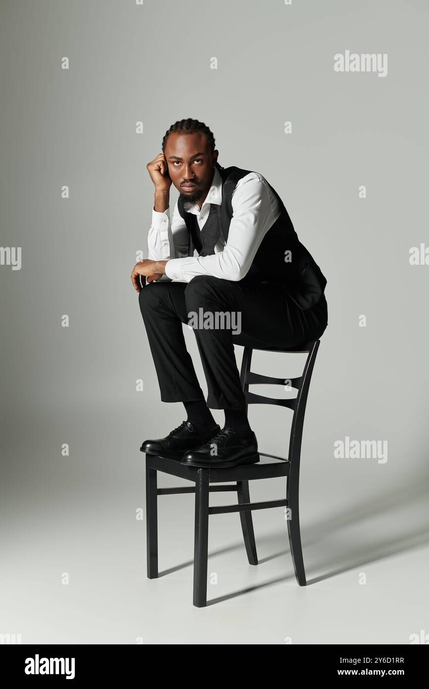 Un jeune homme afro-américain vêtu d'un costume pointu s'assoit sur une chaise, exsudant confiance et style. Banque D'Images