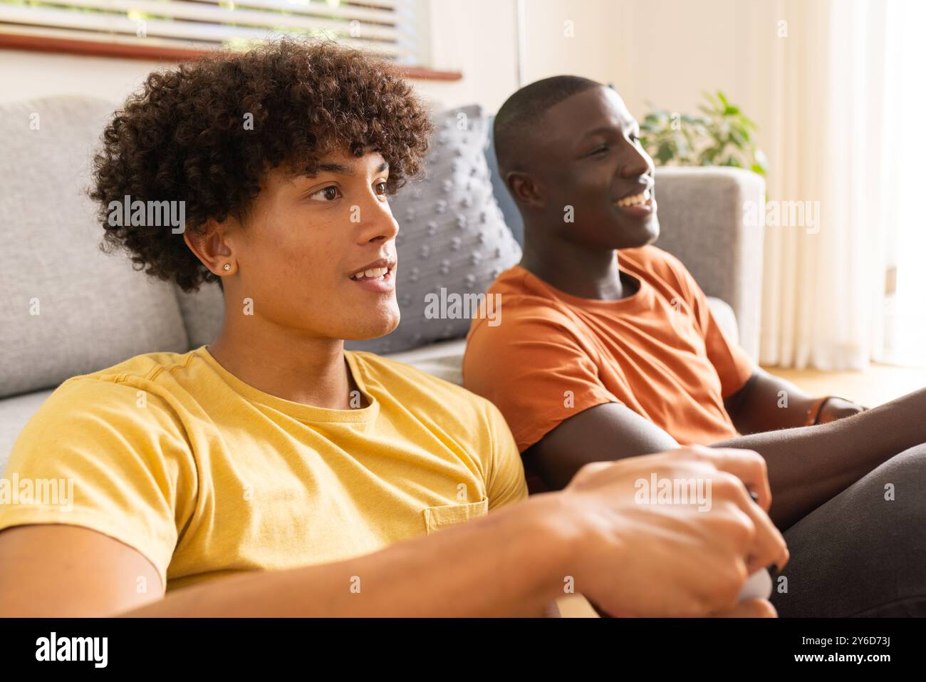 À la maison, jouer à des jeux vidéo, deux jeunes amis masculins divers assis sur le canapé et profiter du temps toge Banque D'Images