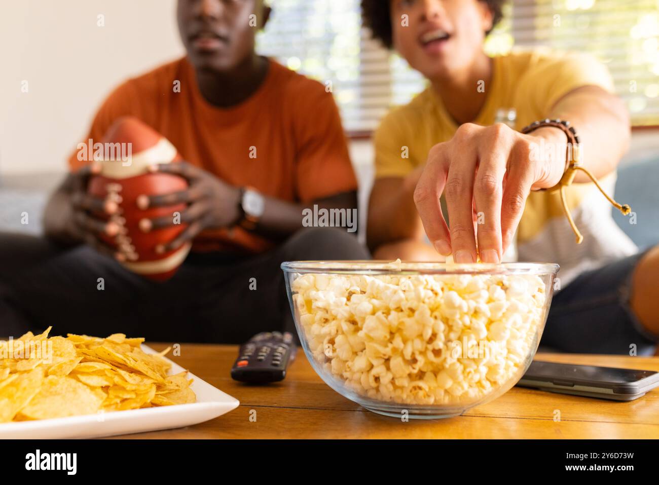 Gros plan, à la maison, regardant le football, deux amis masculins divers mangeant du pop-corn et des chips, profitant de TI Banque D'Images