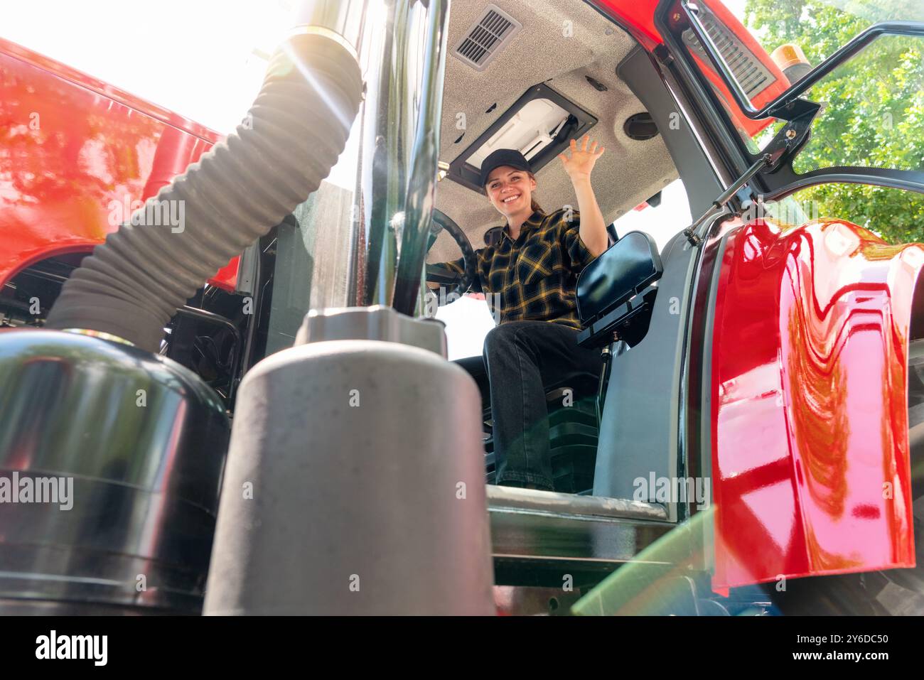 Fermière assise dans la cabine du tracteur souriant et ondulant. Femme conduisant un tracteur agricole ou de construction. Banque D'Images