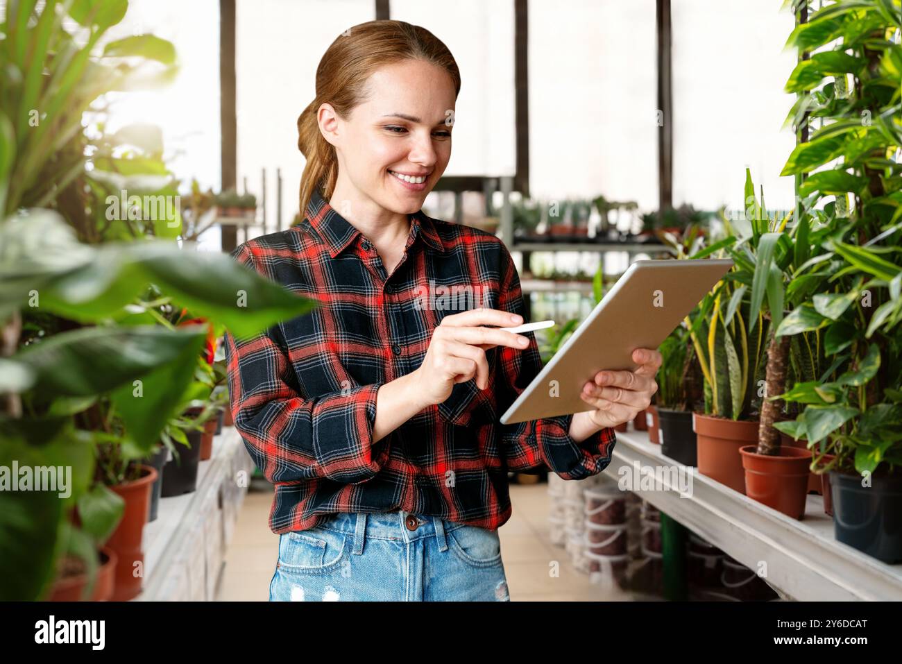 Une femme gère efficacement sa pépinière locale à l'aide d'une tablette numérique, tirant parti de la technologie pour rationaliser le suivi des stocks et améliorer le Cu Banque D'Images