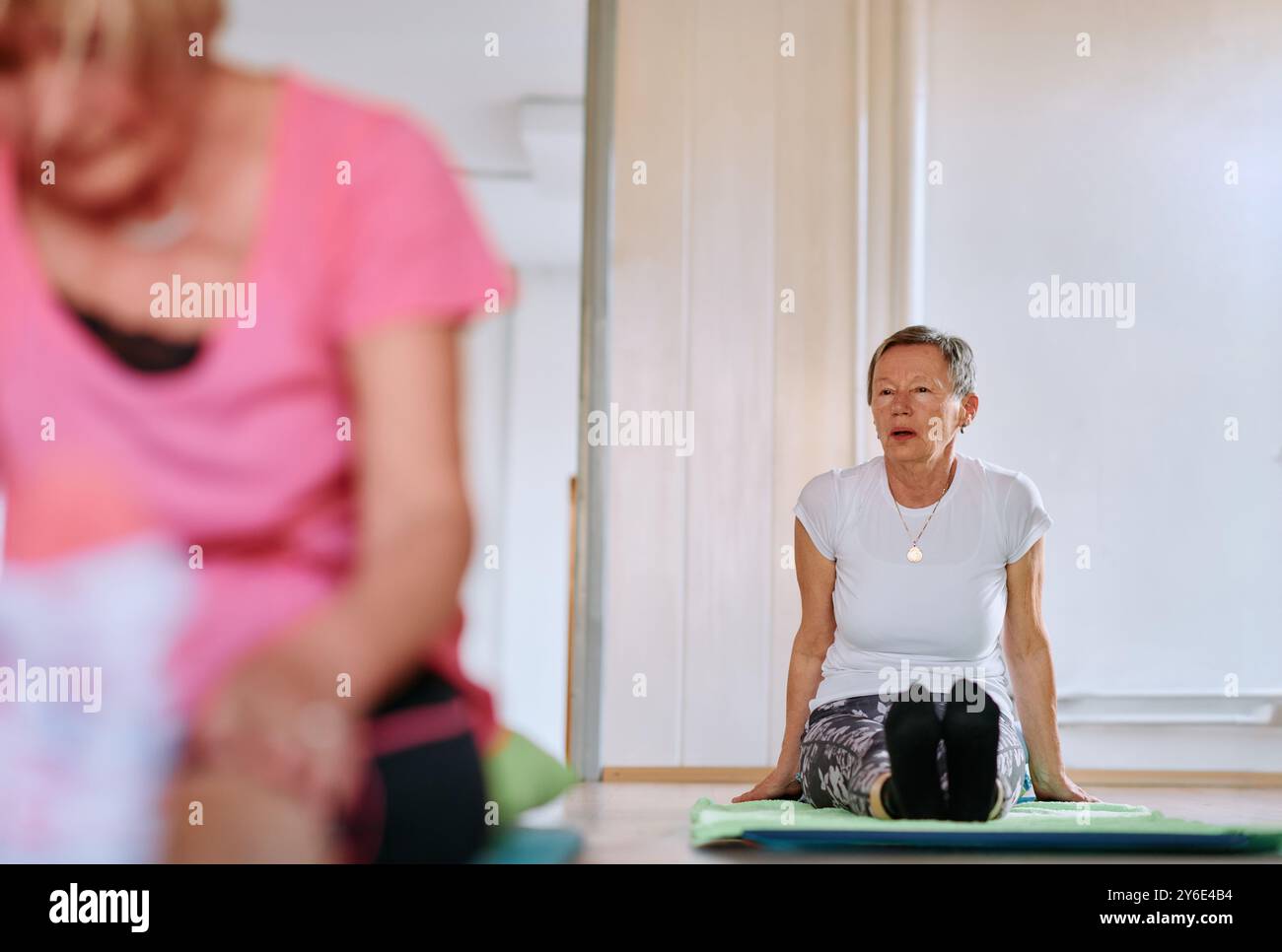 Femme senior pratiquant les étirements de dos dans un espace ensoleillé pour une santé et un bien-être optimaux Banque D'Images