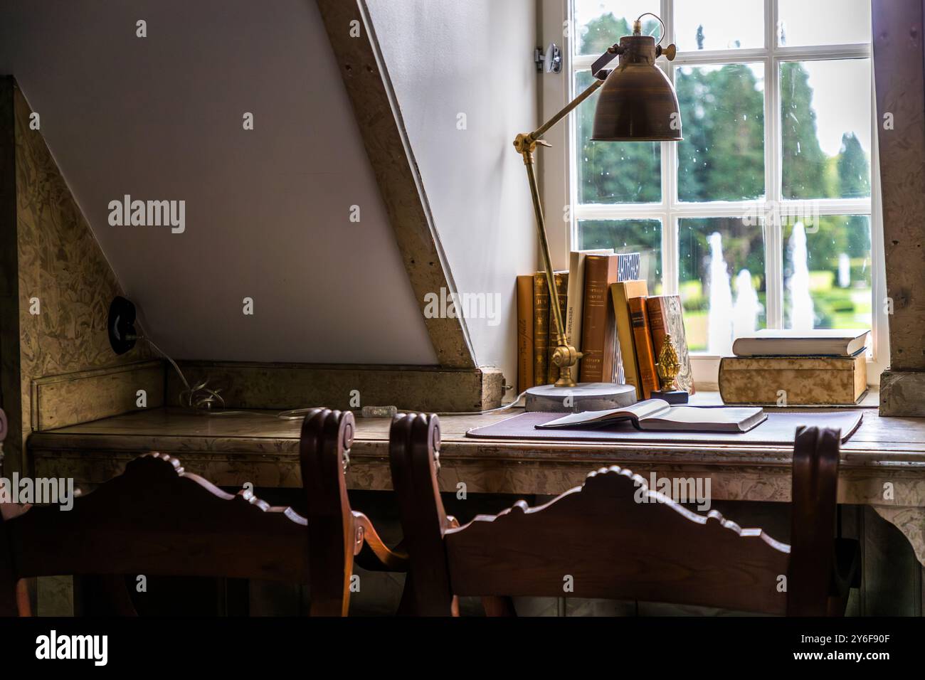 La Villa Abelin abrite un bureau antique avec une lampe en laiton et un livre ouvert sous le plafond incliné à l’étage supérieur, donnant sur une fontaine dans le jardin. Norrvikens trädgårdar, Kattviksvägen, Båstads kommun, Skåne, Suède. Banque D'Images