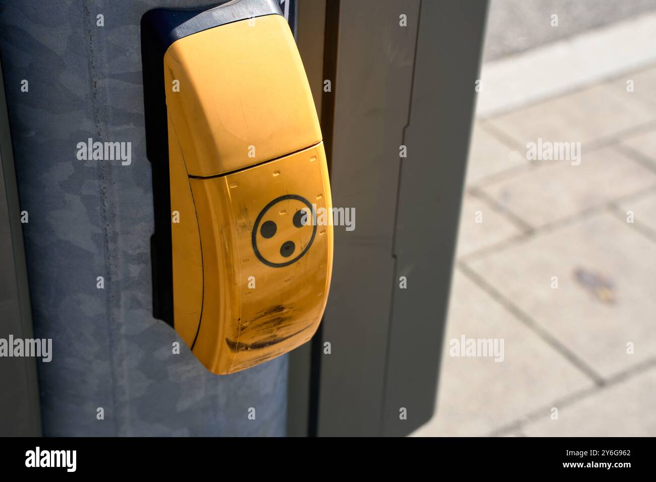 Munich, Bavière, Allemagne - 23 septembre 2024 : un bouton jaune de feu de circulation à un passage à niveau, avec une surface usée, monté sur un poteau métallique, permet aux piétons de demander le feu de circulation *** Ein gelber Ampeldrücker an einer Oberfläche, mit abgenutzter Straßenkreuzung, montiert an einem Metallpfosten, ermöglicht Fußgängern das Anfordern der Ampelschaltung Banque D'Images