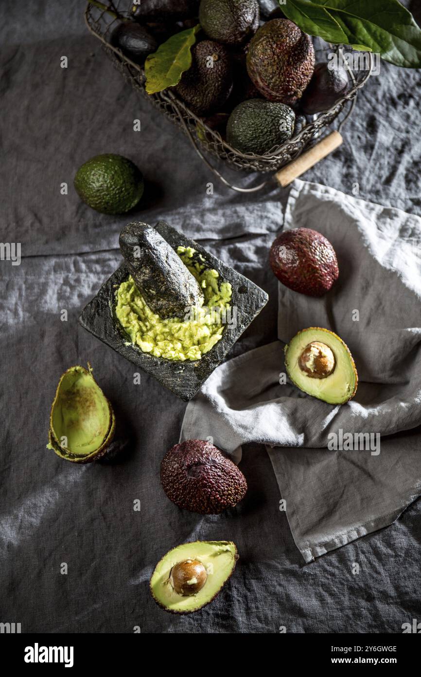 Nourriture, avocat. Guacamole. Sauce guacamole mexicaine dans mortier de pierre, panier plein avec avocat, moitié d'avocat sur nappe de lin. Vue de dessus. Copier l'espace Banque D'Images
