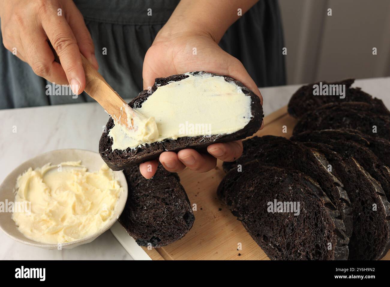 Une femme étale du fromage à la crème avec un couteau à coutellerie en bois sur le pain Chocolate Sourdough. Mains de femme étalant la crème fromage sur la tranche de pain. Banque D'Images