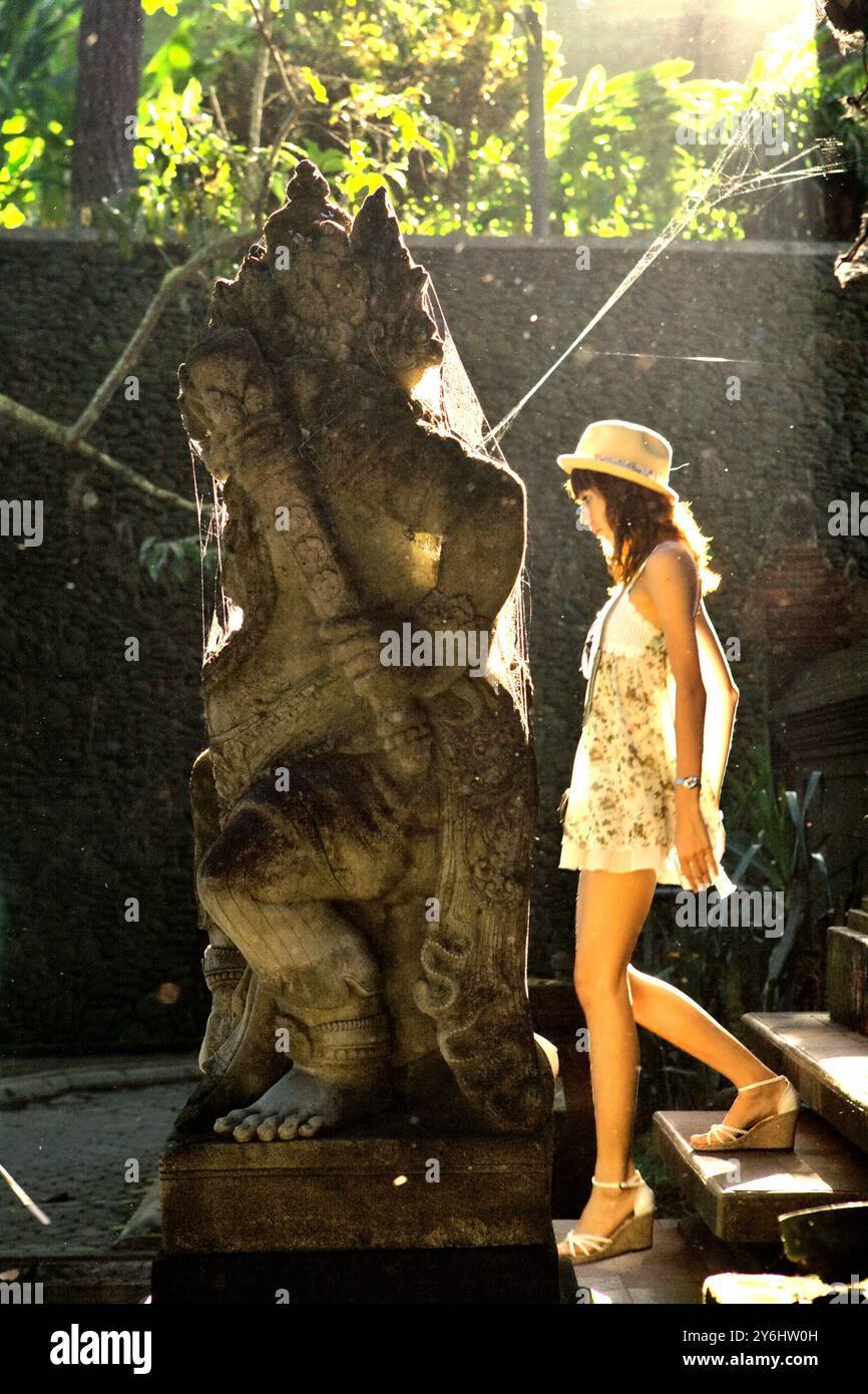 Une femme touriste marchant derrière une statue de dvarapala au complexe du temple Tirta Empul à Tampaksiring, Gianyar, Bali, Indonésie. Banque D'Images