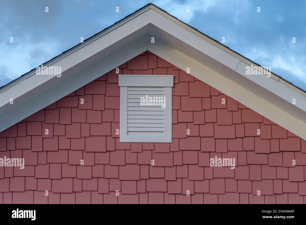 Vue rapprochée du toit de Gable recouvert d'un revêtement en vinyle rouge mat de Cedar Shake et d'un évent de pignon en PVC blanc sur une nouvelle maison américaine avec fond de coucher de soleil Banque D'Images