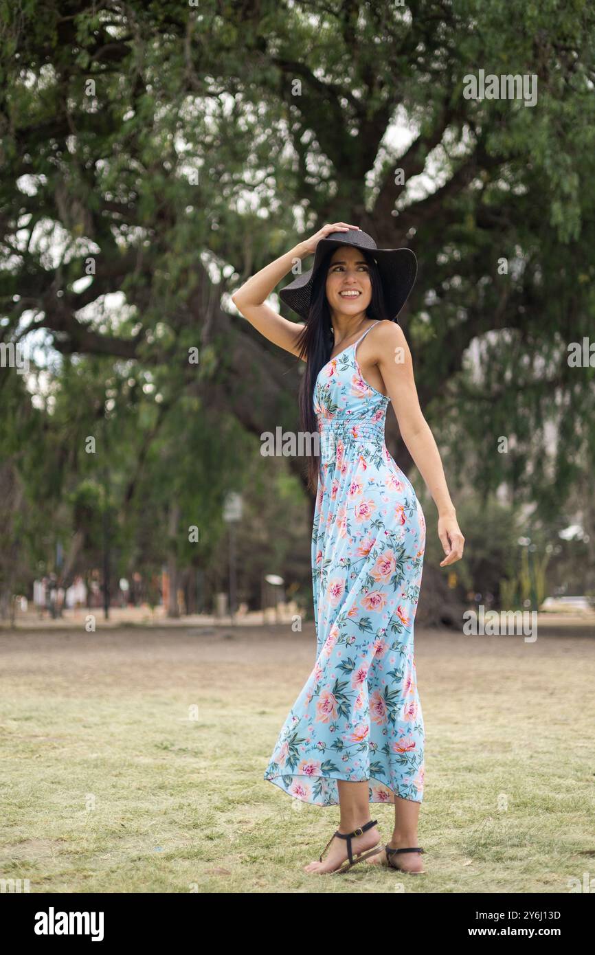 modèle féminin attrayant avec une beauté naturelle en portrait, porter une longue robe imprimée et un chapeau pour l'été, papier peint avec la nature en arrière-plan Banque D'Images