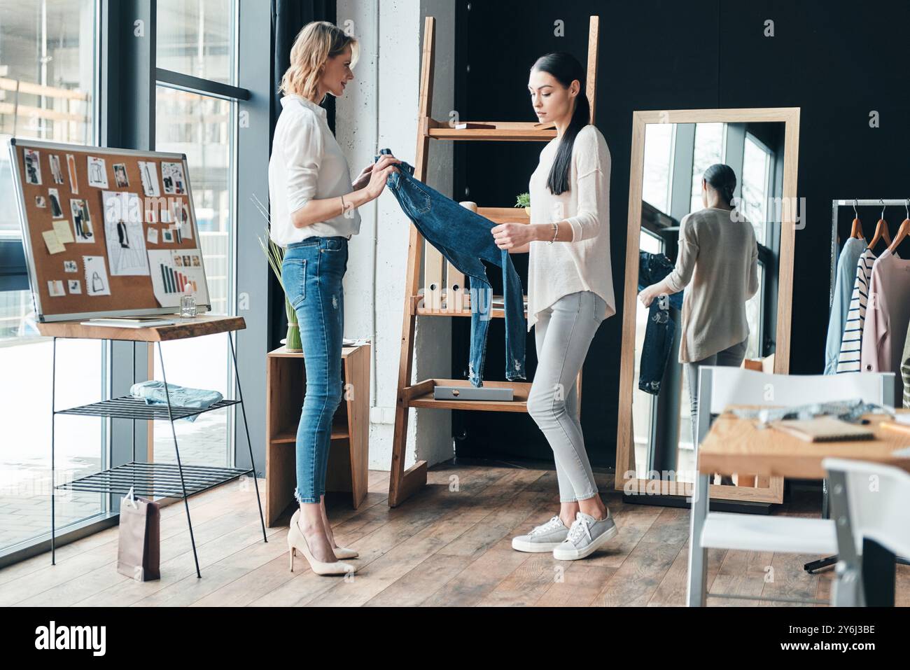 Développer une nouvelle ligne de mode. Pleine longueur de belles jeunes femmes tenant un Jean et le regardant tout en passant du temps dans l'atelier Banque D'Images