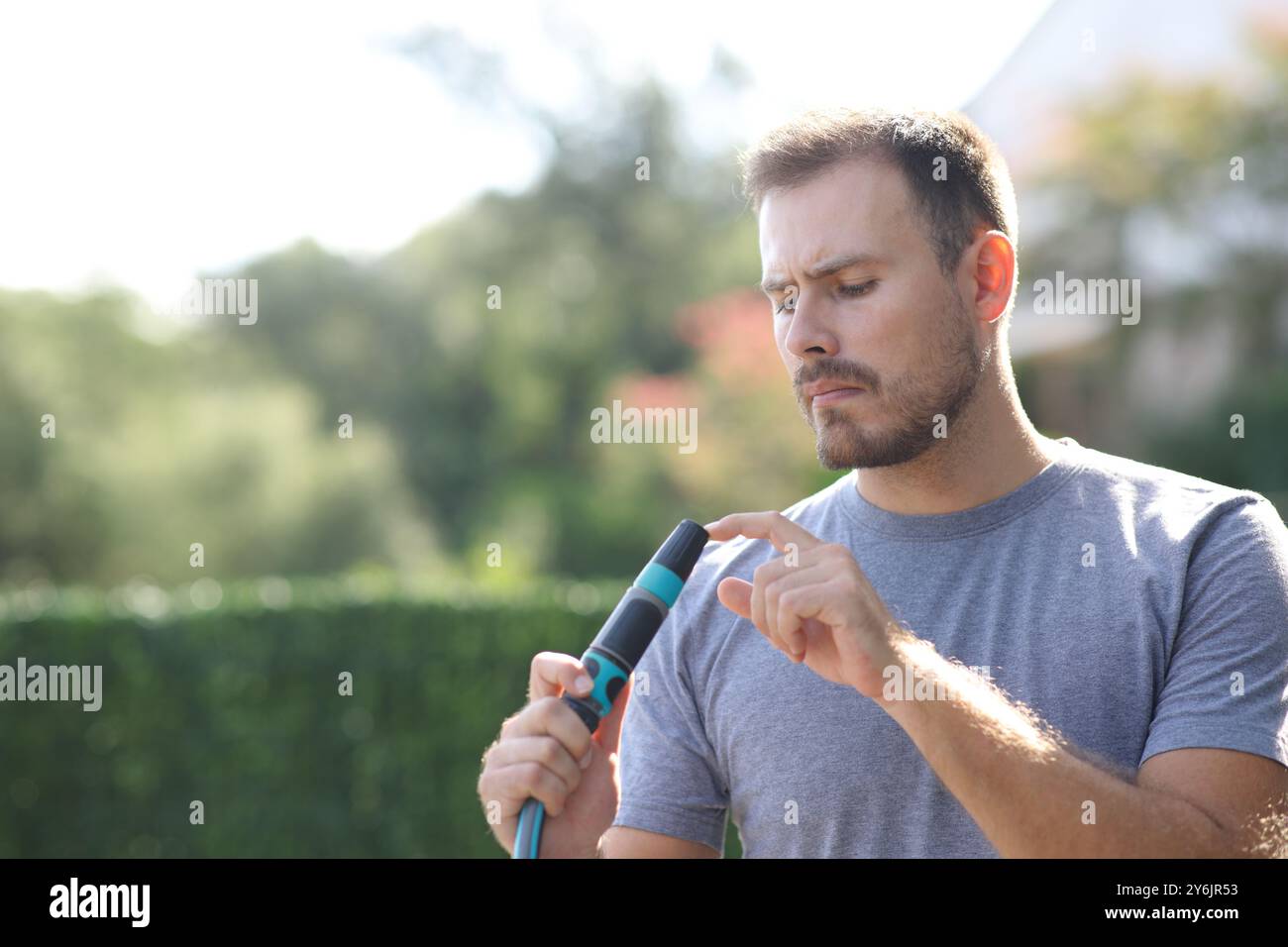 Homme confus regardant la buse de tuyau bouchée dans un jardin Banque D'Images