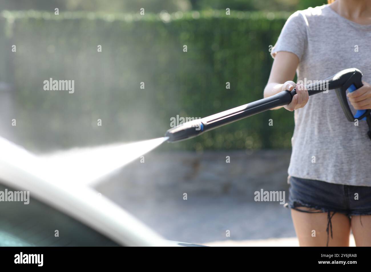 Gros plan d'une femme lavant la voiture avec de l'eau en utilisant une laveuse à haute pression dans le jardin à la maison Banque D'Images