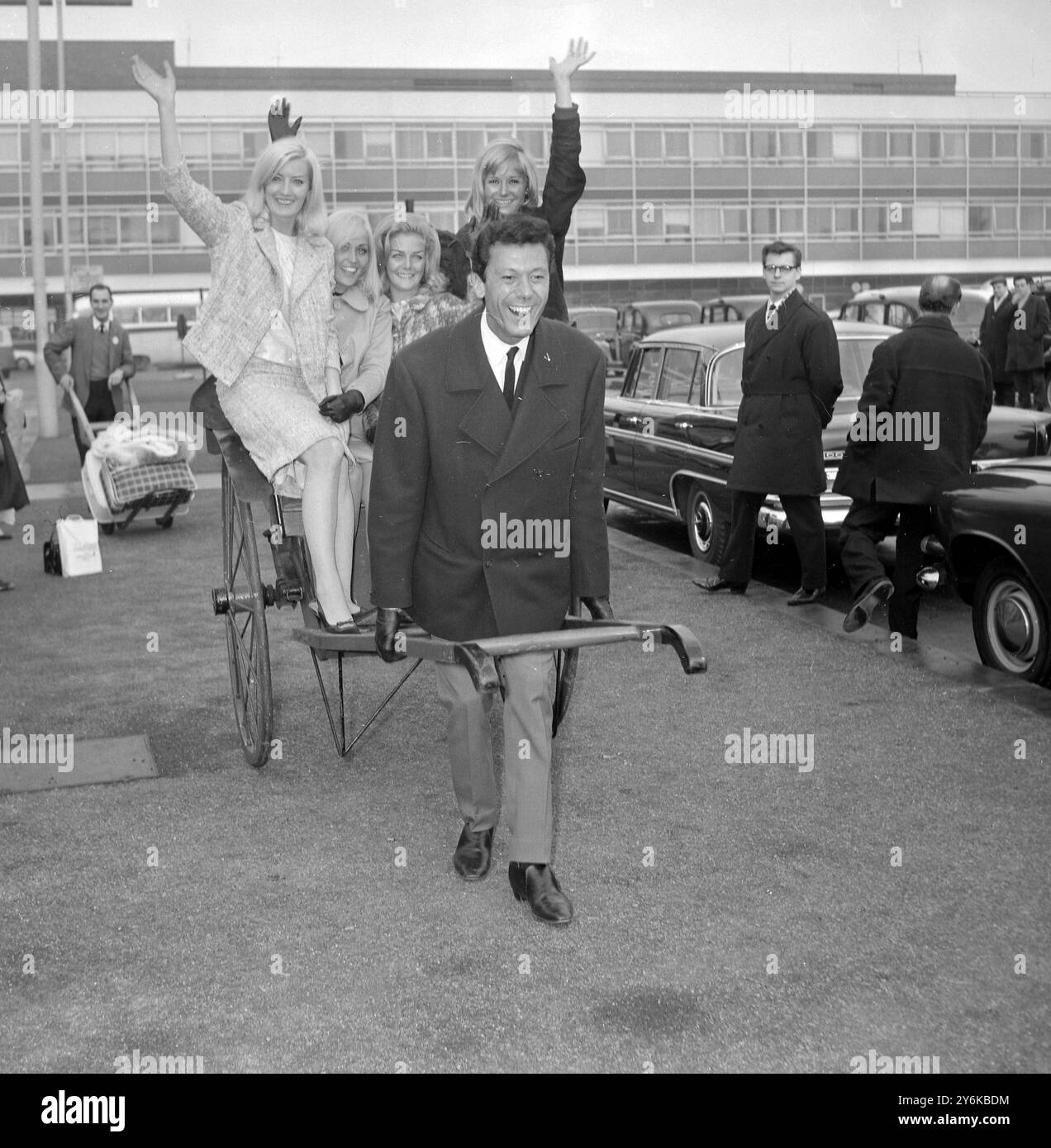 Aéroport de Londres : le danseur et chorégraphe Lionel Blair transporte le long d'un pousse-pousse contenant la danseuse, de gauche à droite, Dianna Williams, Jackie Irving, Eithne Milne et Jennifer à droite, à leur arrivée à l'aéroport de Londres aujourd'hui. Lionel et les filles qui sont les 'danseurs Lionel Blair' sont rentrés de Hong Kong et Singapour où ils jouent depuis deux mois. Le mois prochain, ils jouent dans une nouvelle série ITV. 1er février 1965 Banque D'Images