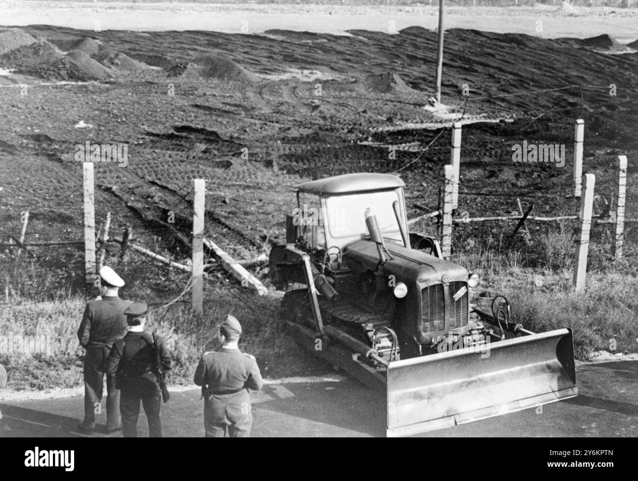 Berlin : un bulldozer est coincé dans la clôture de barbelés sur la Klemke Strasse à la frontière du secteur français ici, le 18 octobre, après qu'un garde-frontière est-allemand ait fait son chemin vers la liberté. Le garde de 22 ans travaillait au nivellement du sol du côté est de la frontière (en arrière-plan), pour priver les réfugiés de couverture et fournir aux gardes un champ de tir dégagé. Il a soudainement tourné le tracteur vers la clôture et a fait un passage au bulldozer. Un racleur équipé du tracteur a aidé à couper le fil barbelé. 21 octobre 1963 Banque D'Images