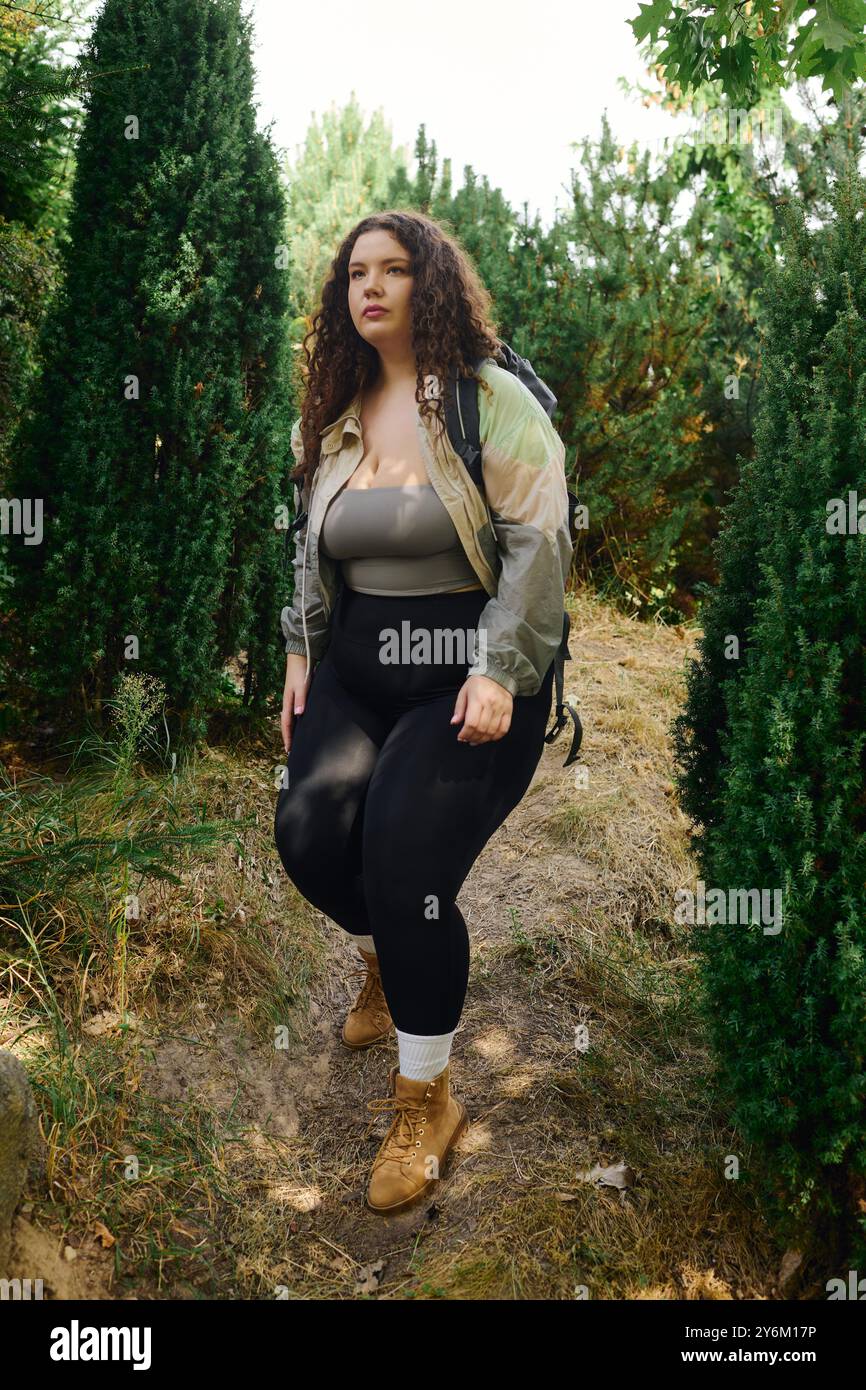 Une femme de taille plus confiante profite d'une promenade paisible parmi les arbres verts vibrants. Banque D'Images