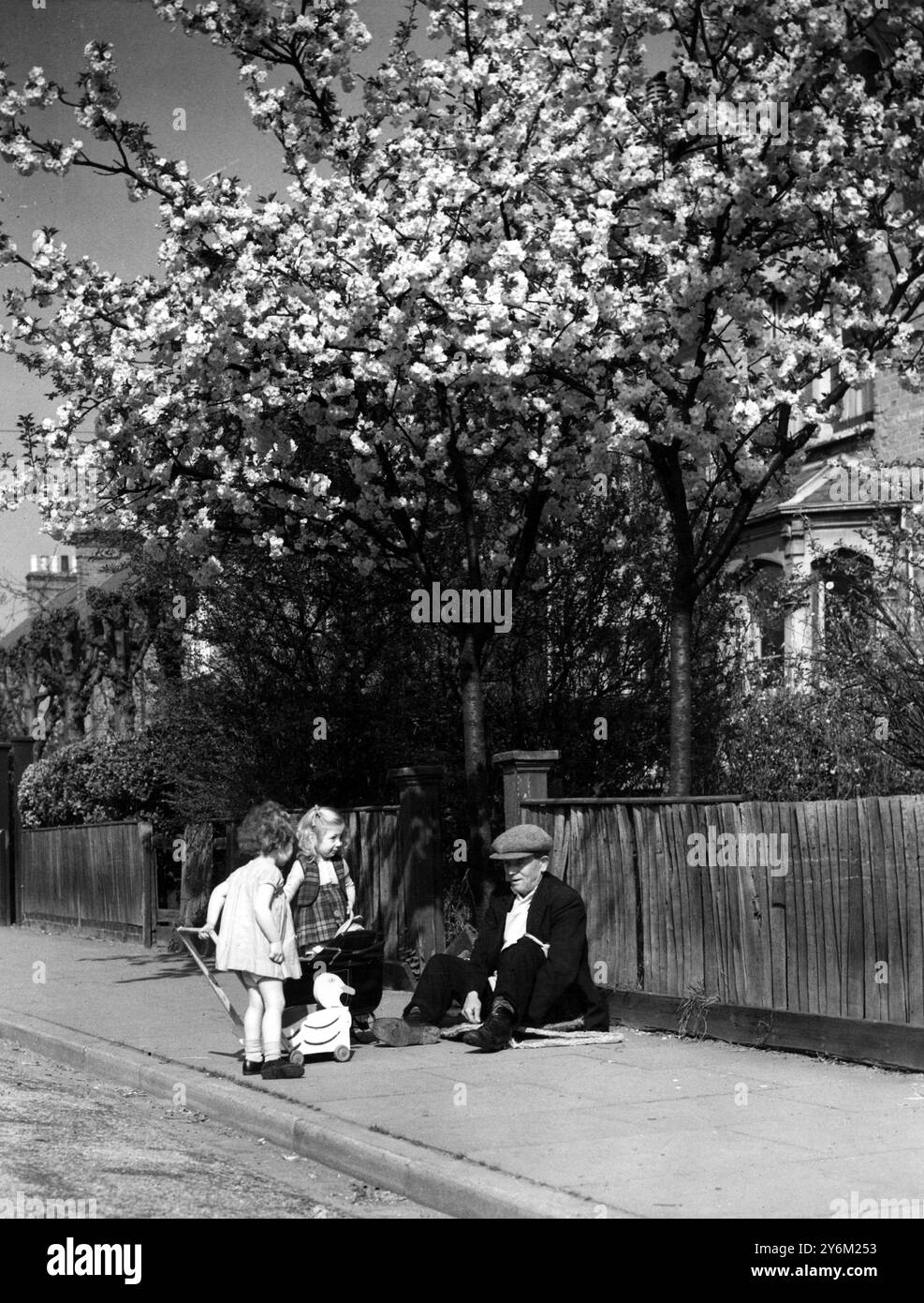 Un vieil homme assis sur le trottoir discute avec deux petites filles espiègles. Banque D'Images