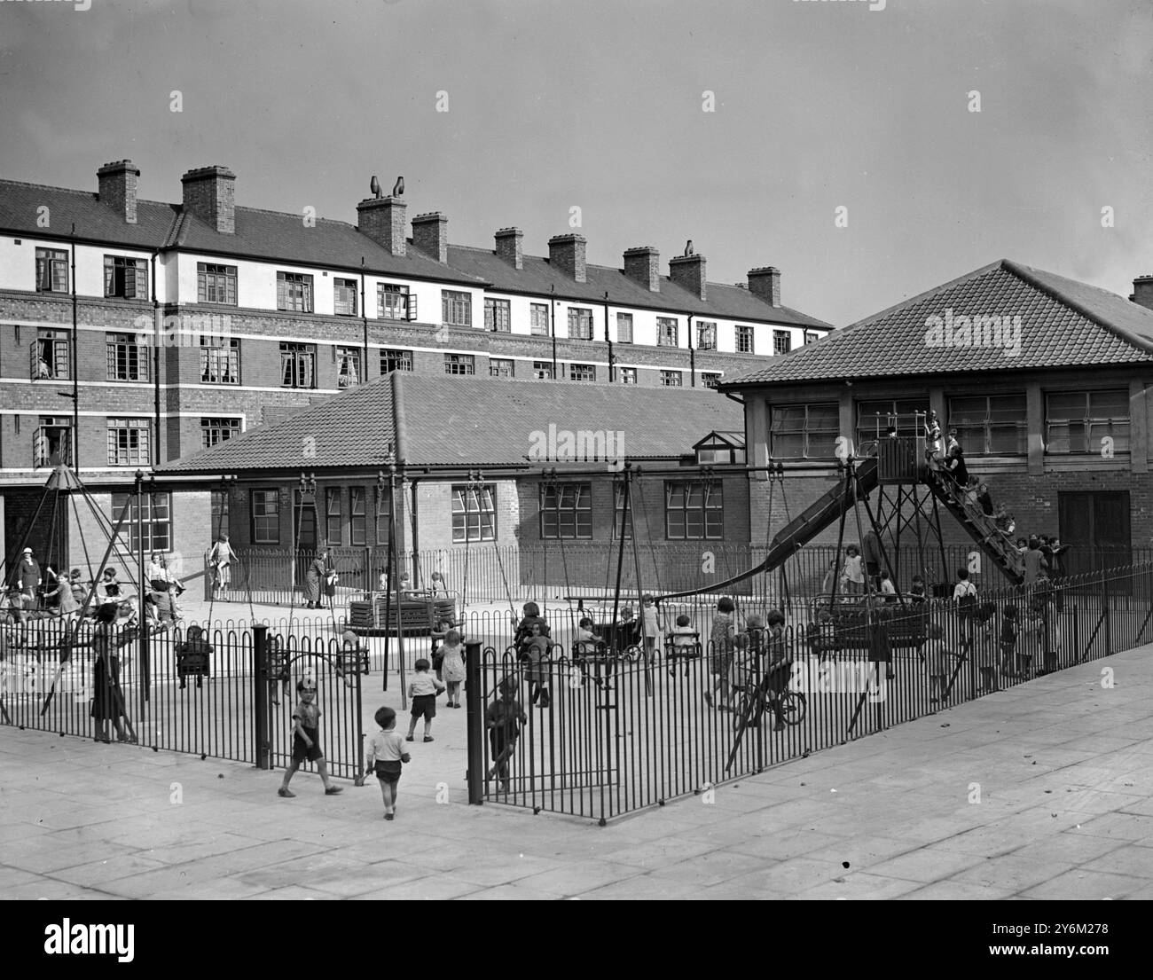 Enfants jouant dans une aire de jeux du centre-ville. Nouveau bloc d'appartements avec des fenêtres de critères en arrière-plan. Garde-corps et trottoirs au premier plan. Peut-être dans le sud ou l'est de Londres. Probablement publié le 20 juillet 1938 Banque D'Images