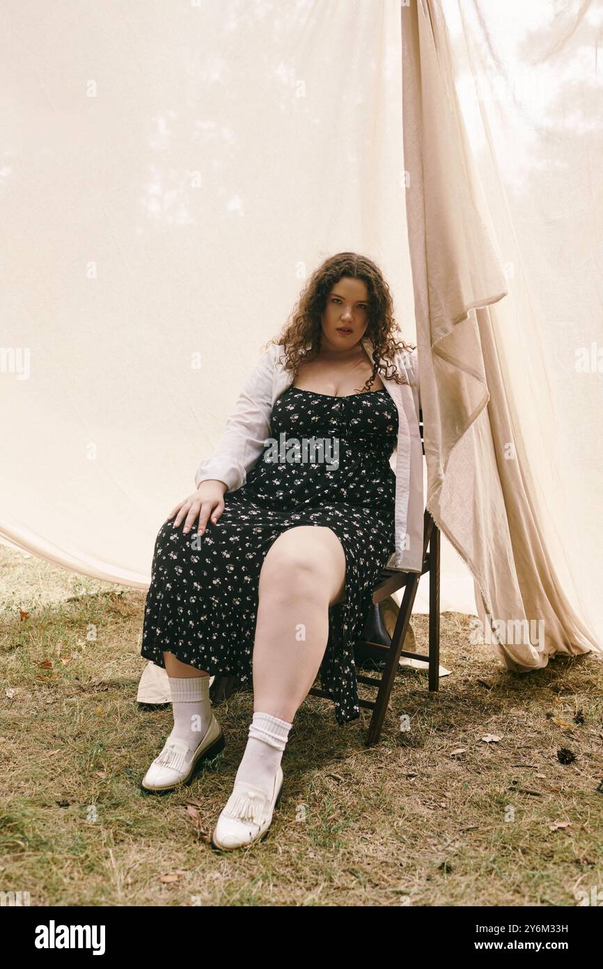 Une femme de taille plus dans une robe florale se détend dans un champ tranquille sous la lumière douce du soleil. Banque D'Images