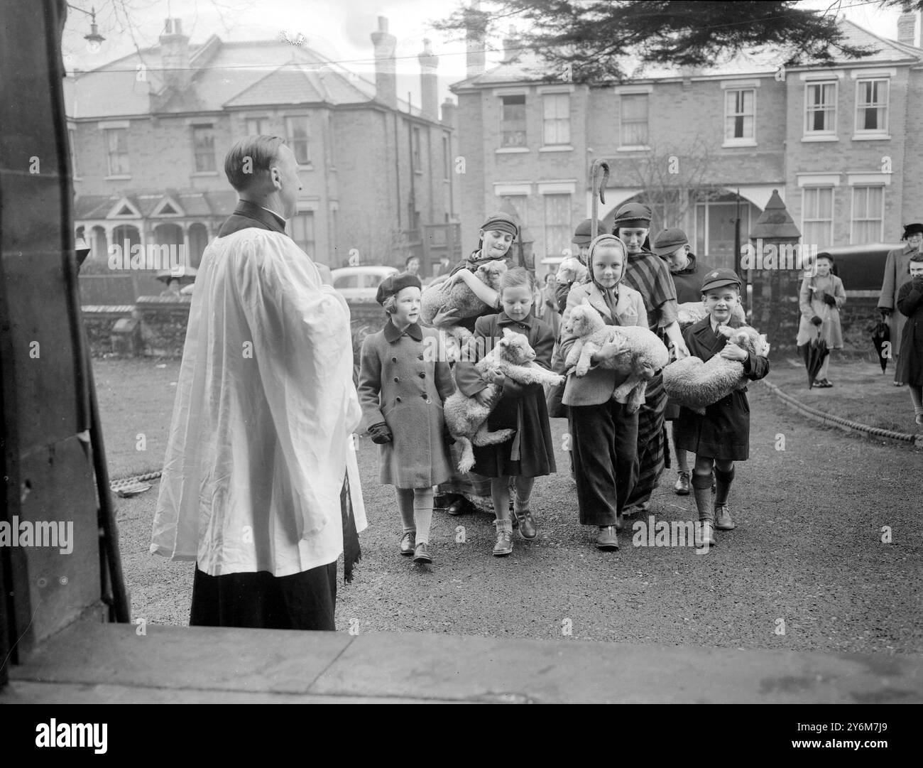 Bromley, Kent le révérend John Rahe Hughes, vicaire de l'église St Mary, Bromley, se tient à la porte de son église pour accueillir les enfants qui apportent des agneaux à un service spécial pour les enfants. Six agneaux, âgés de seulement deux ou trois semaines, ont été prêtés par une ferme du Kent pour illustrer le thème du service spécial, «le bon Pasteur - - les agneaux ont dû être de retour avec leurs mères dans les deux heures. - - 5 avril 1953 Banque D'Images