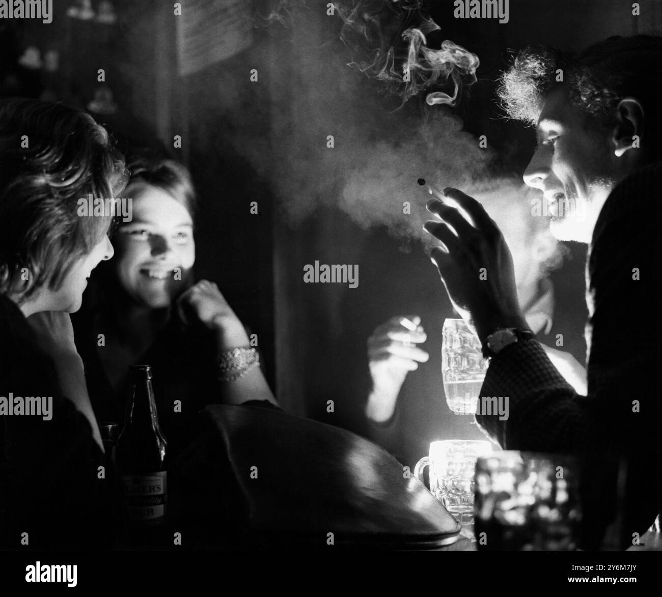 Hommes et femmes fumant et buvant de la bière dans un pub 1961 Banque D'Images
