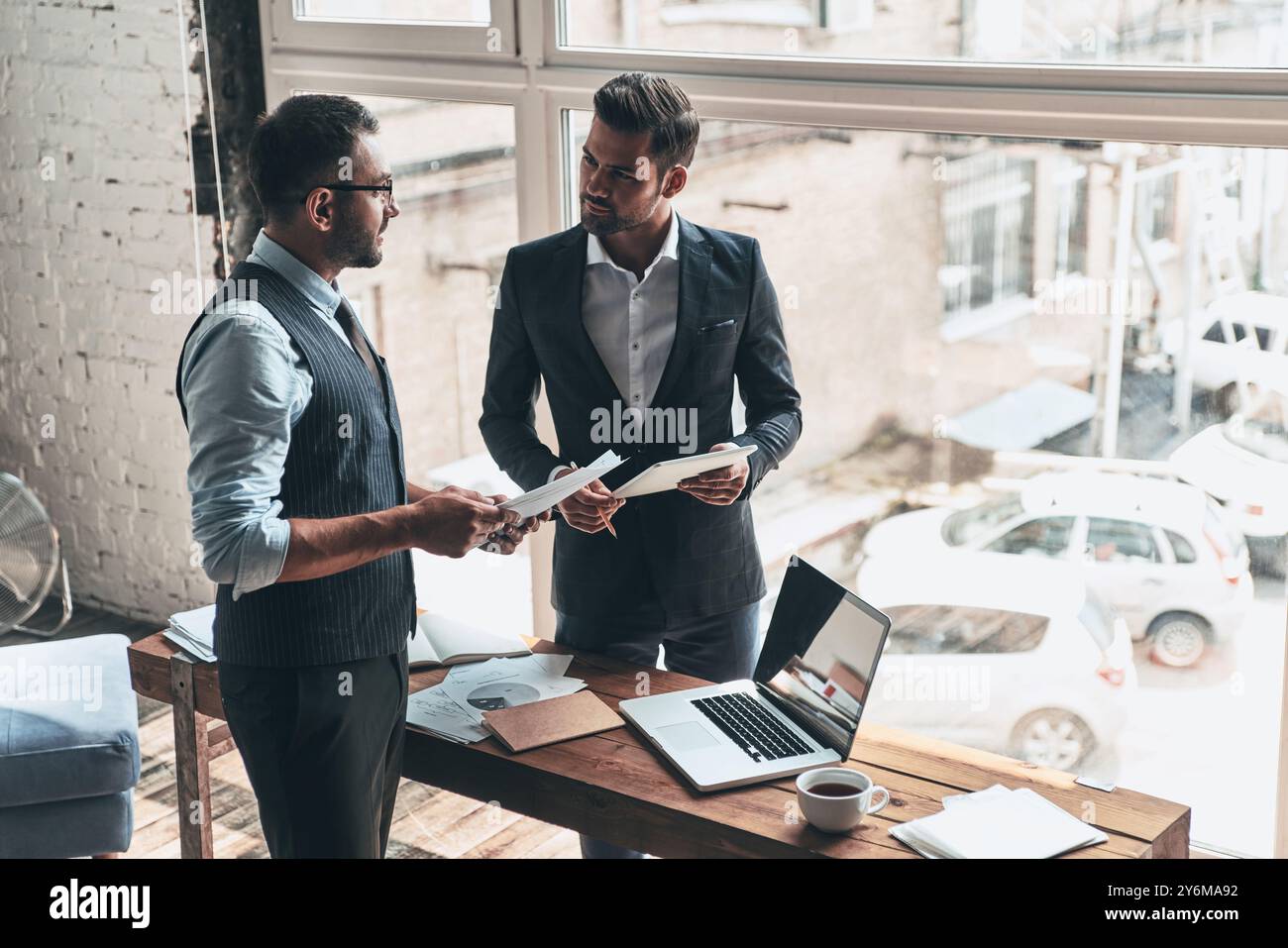 En passant en revue les détails. Vue de dessus de deux jeunes hommes modernes en vêtements de forme travaillant ensemble tout en restant debout à l'intérieur Banque D'Images