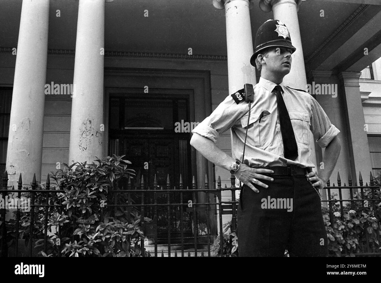 Un policier en manches chemises se tient sur la garde devant l'ambassade d'Espagne à Belgrave Square, Knightsbridge. La police a été appelée à se rendre dans le bâtiment à la suite d'un attentat à la bombe. La porte de l'ambassade (vue en arrière-plan) montre des preuves de l'attaque. Une bouteille de whisky remplie d'essence explosa sur le pas de la porte, brûlant la peinture. 7 juillet 1969 Banque D'Images