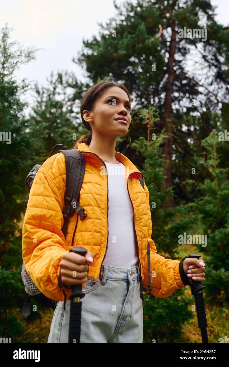 Au milieu du feuillage d'automne coloré, une femme explore la forêt avec confiance avec des bâtons de randonnée à la main. Banque D'Images