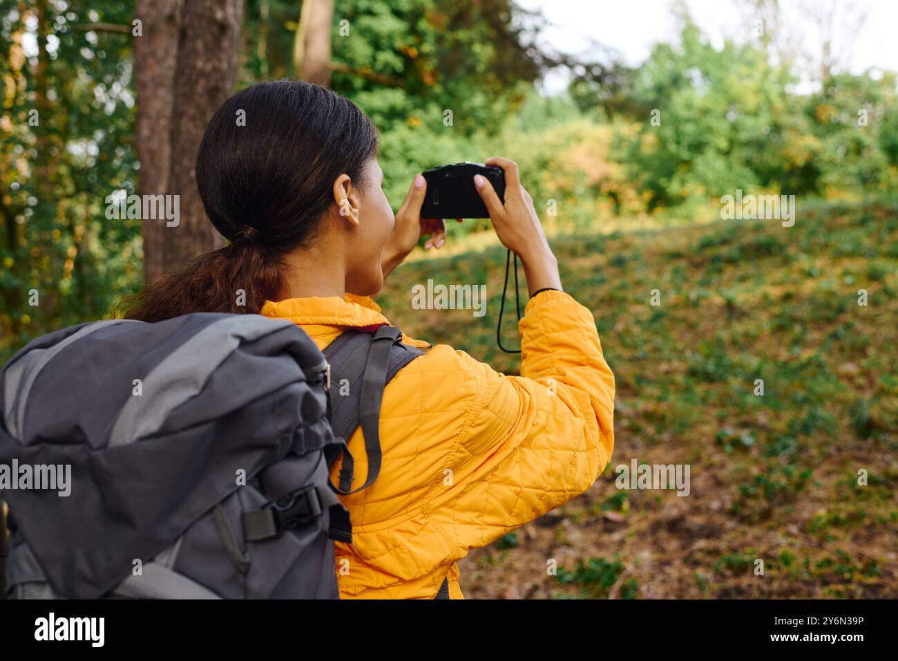 Une jeune femme afro-américaine avec un sac à dos prend un moment pour capturer les couleurs de l'automne tout en faisant de la randonnée. Banque D'Images