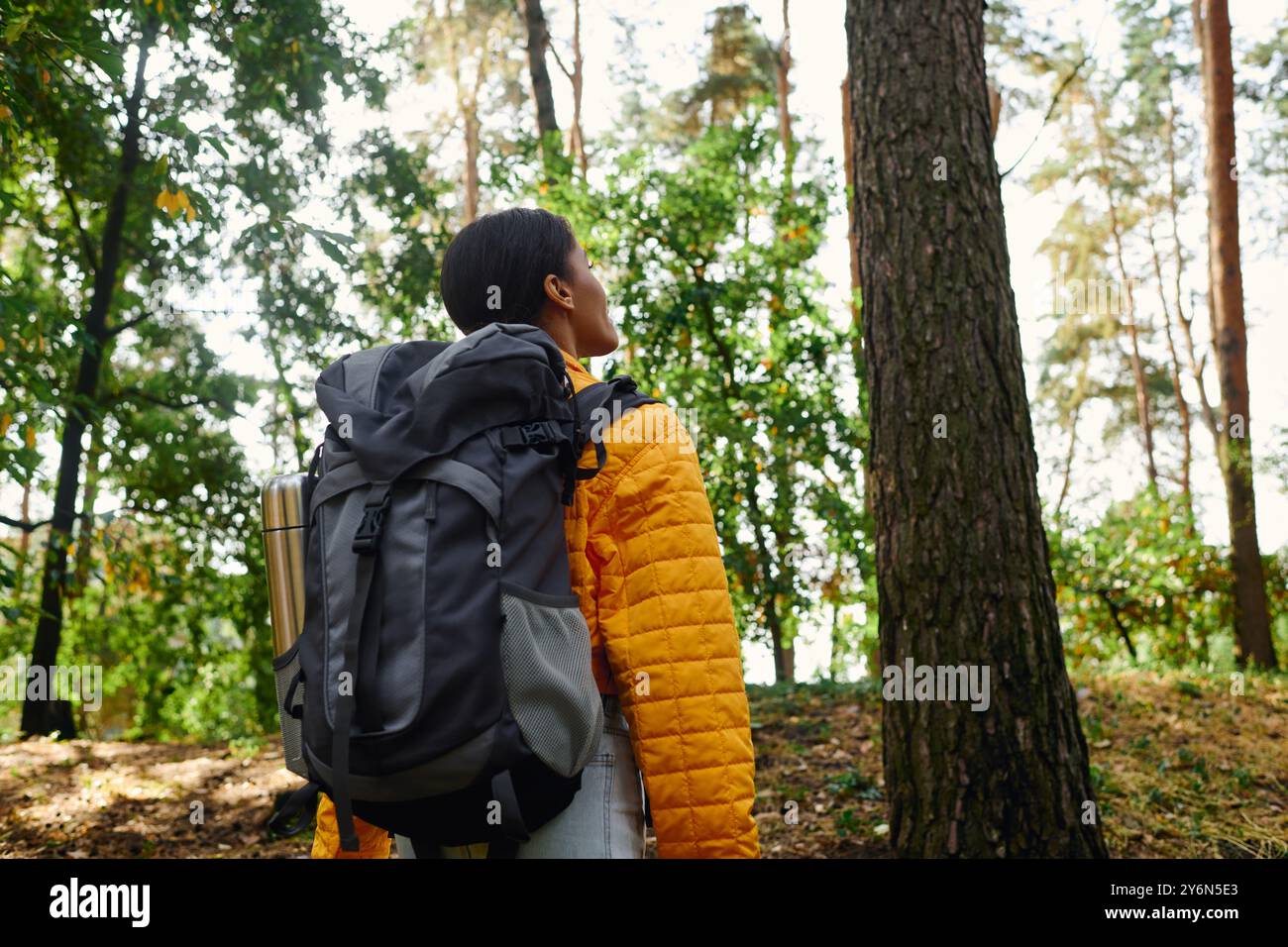 Une jeune femme afro-américaine profite de sa randonnée à travers une forêt riche et colorée dans la lueur chaude de l'automne. Banque D'Images